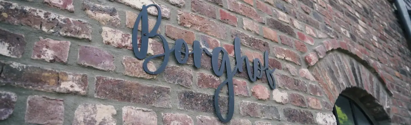 Der Schriftzug „Borghof“ aus dunklem Metall an der alten Backsteinwand