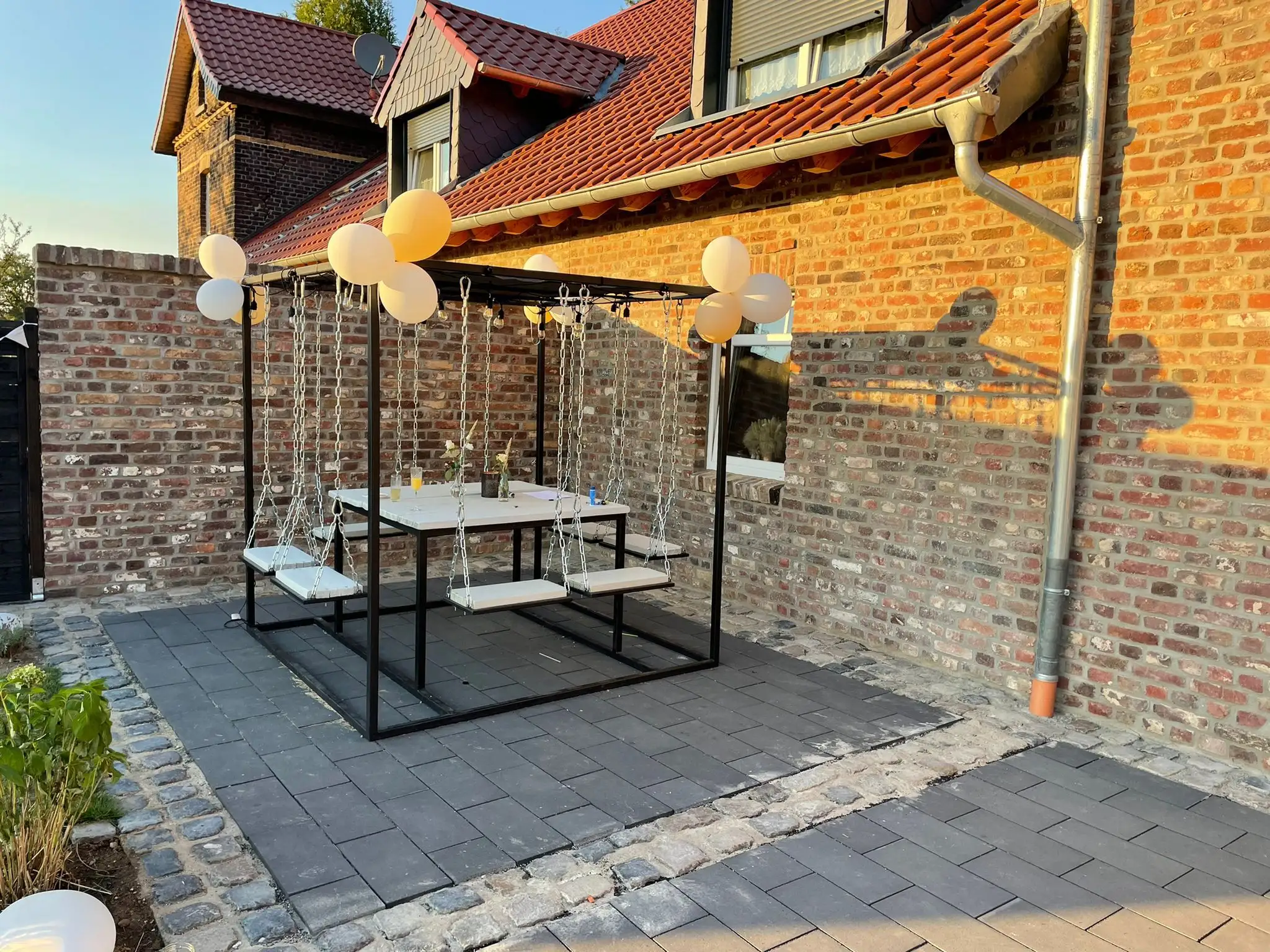 Schaukelbank und Sitzgruppe auf der gepflasterten Terrasse, dekoriert mit Ballons