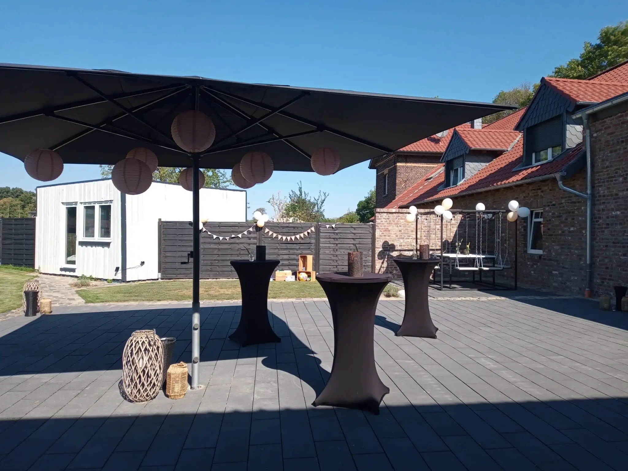 Terrasse mit großem Sonnenschirm, Stehtischen und Lichterketten